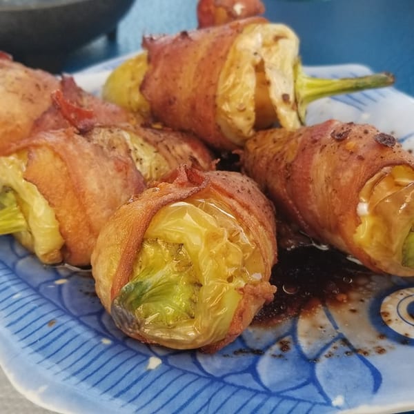 Bacon-wrapped peppers with a savory sauce on a blue and white fish-shaped plate.