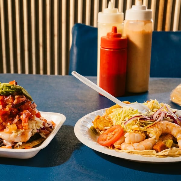 Shrimp tostadas and tacos with various toppings on a blue table with condiments.