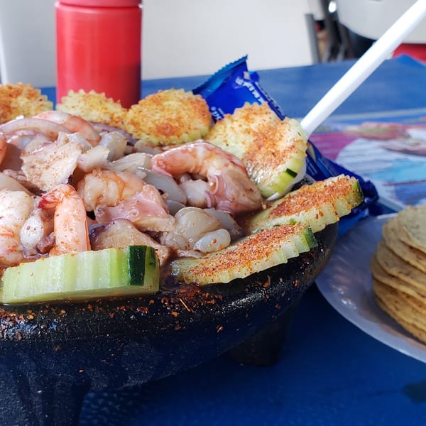 A molcajete bowl filled with shrimp, octopus, cucumber, and chili powder, with a side of tortillas.