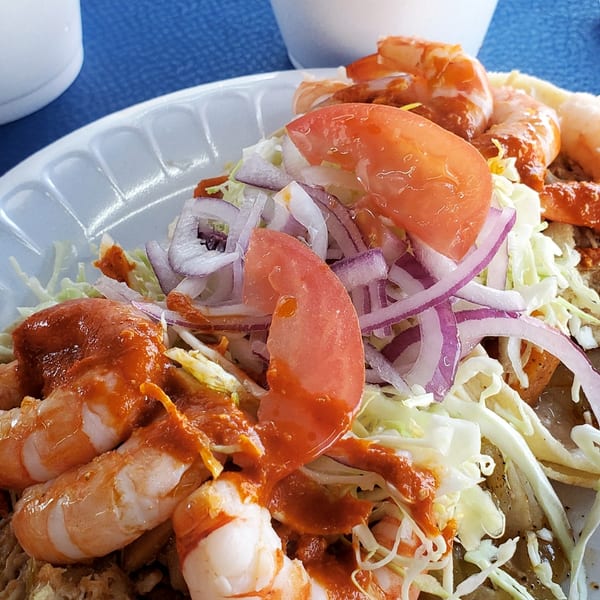 Shrimp tacos with cabbage, red onion, and tomato, served with a side of soup.