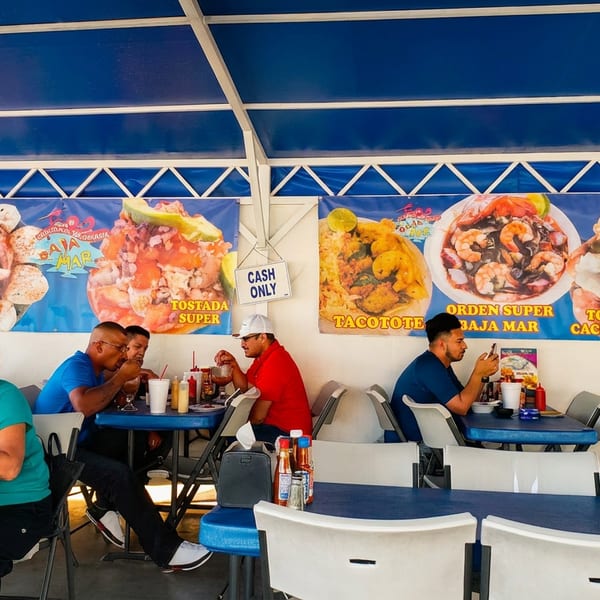 People dining under a blue canopy with large seafood menu banners on the wall.